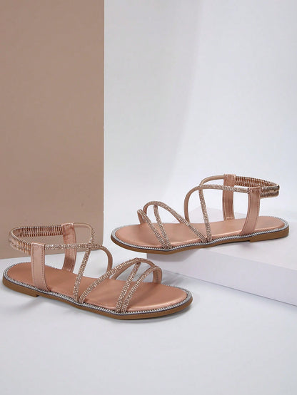 صنادل مسطحة برأس مدور وتفاصيل معدنية ومرصعة بالراين، حزام كاحل مطاطي، استيل روماني للنساء