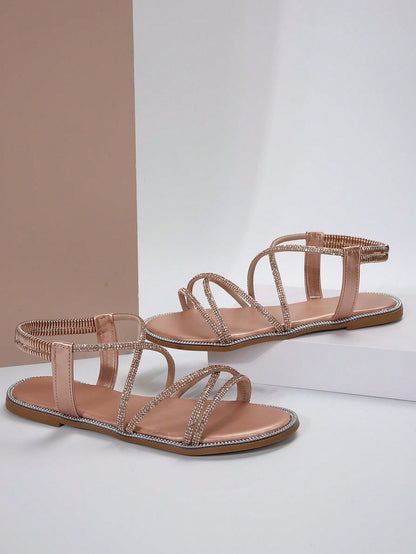 صنادل مسطحة برأس مدور وتفاصيل معدنية ومرصعة بالراين، حزام كاحل مطاطي، استيل روماني للنساء